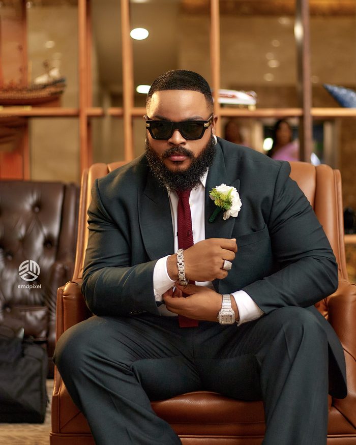 Whitemoney in a charcoal suit with a boutonniere, seated